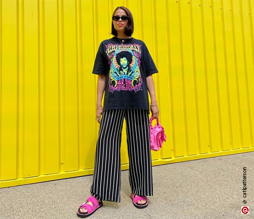 Model wearing black top and pants with pink bag and sandals